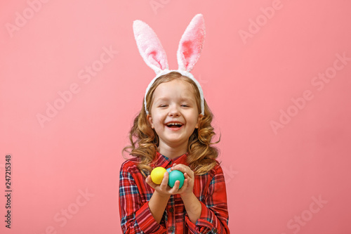 Photography Cheerful little kid girl with bunny ears with easter eggs on a colored background