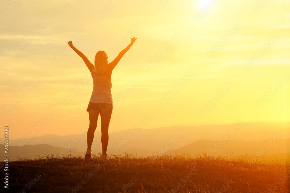 Happy woman traveler with open arms stay on the peak of mountain in sunset