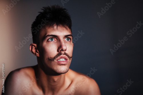 Young shirtless man with mustache thinking by the window