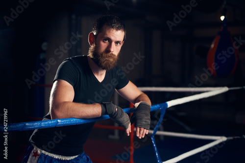 Portrait of young male professional boxer standing in the ring at the health club after hard training boxing