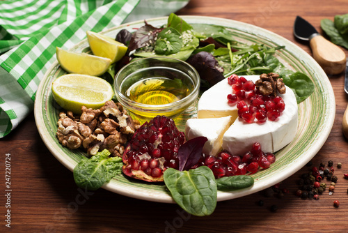 Soft Camembert cheese, pomegranate seeds, mix salad with young spinach, arugula, beet leaves, lime and nuts on a green plate. Tasty, gourmet food