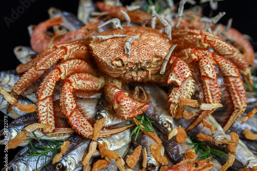 Big hairy boiled crab sits on a heap of dried salted fish on a gift bouquet on the black background, close-up