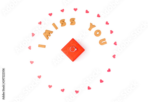 Valentine's day concept. Text I MISS YOU from cookies, frame made of paper hearts. In the center red gift box with ring. Flat lay, top view, white background, isolated, copy space