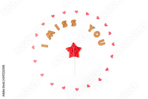 Valentine's day concept. Text I MISS YOU from cookies, frame made of paper hearts. In the center lollipop in form star. Flat lay, top view, white background, isolated, copy space