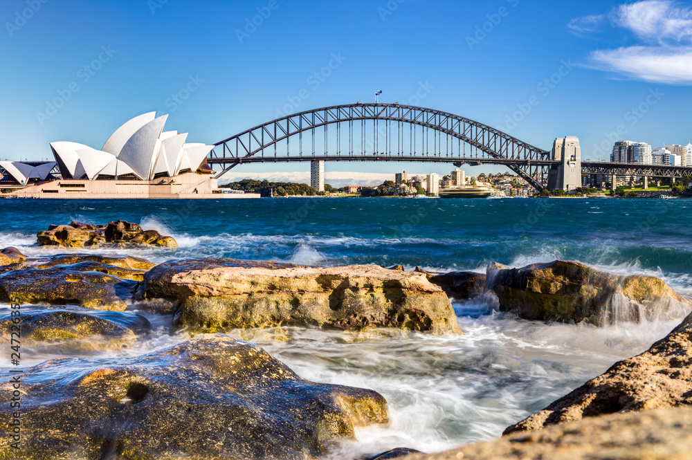Obraz premium widok na port w sydney z operą, mostem i skałami na pierwszym planie