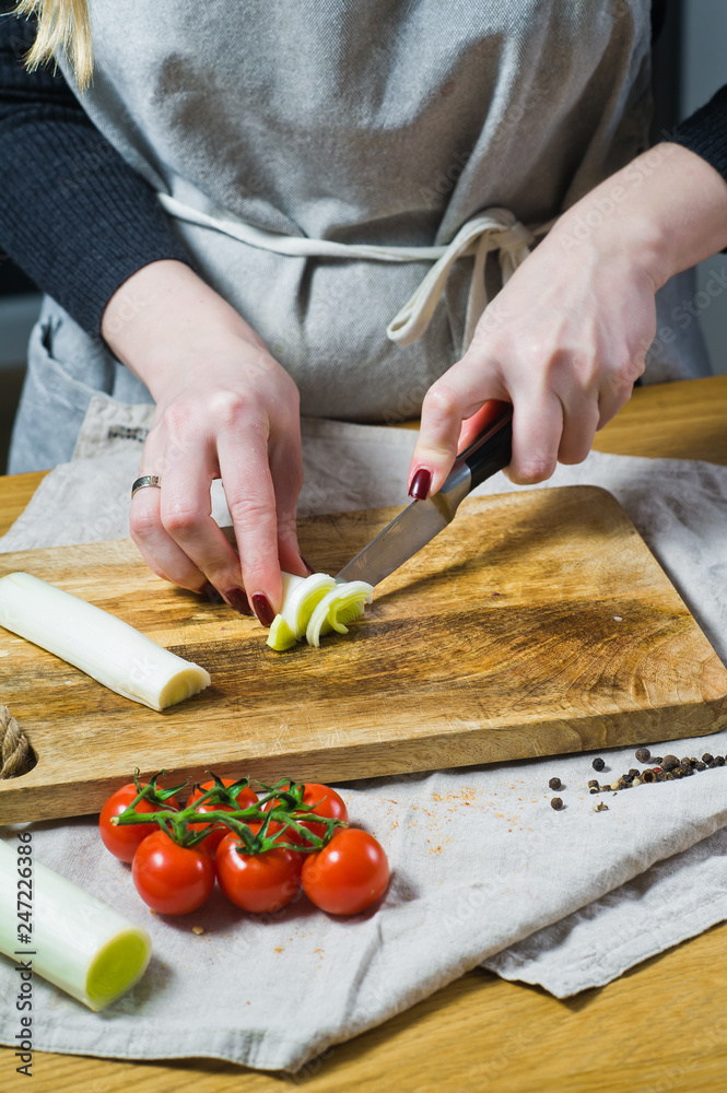 The chef cuts leeks on a wooden chopping Board. Background kitchen, side view
