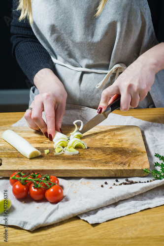 The chef cuts leeks on a wooden chopping Board. Background kitchen, side view