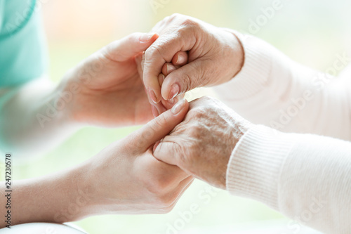 Closeup of hands of young nurse holding hands of an senior lady