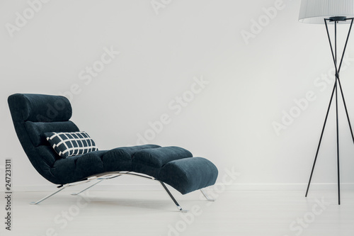 Stylish dark blue settee with checkered pillow next to trendy lamp in neat living room with copy space on empty wall