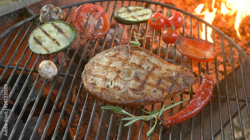 Meat and vegetables on the grill with flames in the background, dish in the restaurant, fish meat on the bone, zucchini, tomatoes, pepper and garlic, healthy way of life