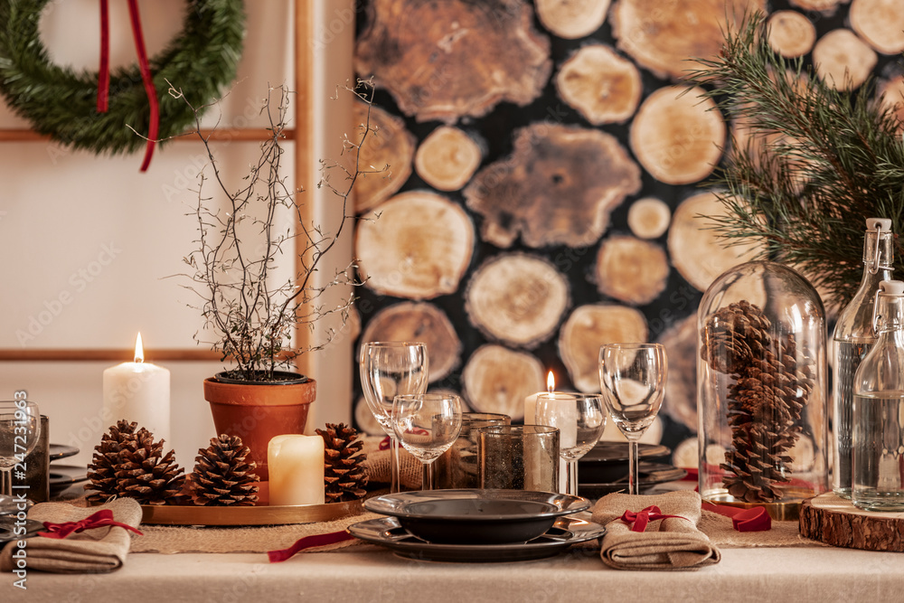 Dining room table set for christmas, wine glasses, cones and black plates on linen tablecloth Dining room table set for christmas, wine glasses, cones and black plates on linen tablecloth