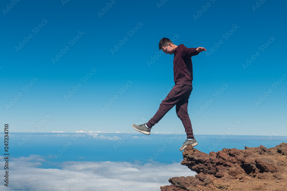 Extreme man standing and balancing on high mountain cliff edge Extreme man standing and balancing on high mountain cliff edge