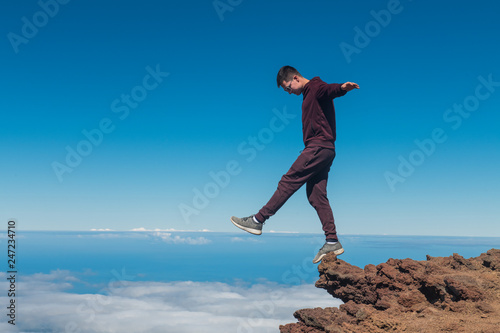 Extreme man standing and balancing on high mountain cliff edge