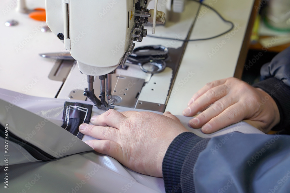 Men seamstress at the sewing machinesews the tarpaulin. Selective focus.