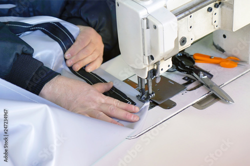 Men seamstress at the sewing machinesews the tarpaulin. Selective focus.