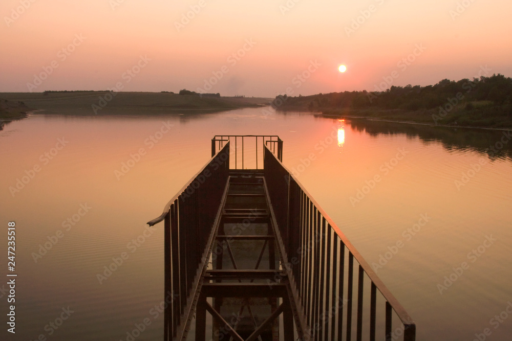 Fototapeta premium Sunset next to the water with broken bridge