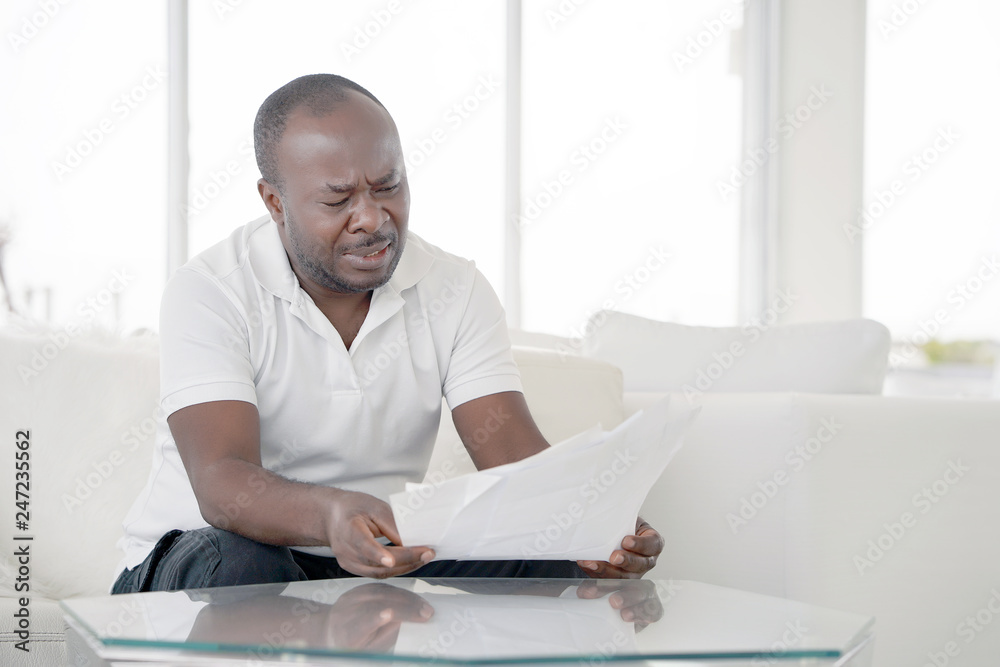 Man reads negative news in a letter at home on the couch. The shaken business manager of the african male received a notice of dismissal from the company, surprised. An agitated man without joy. Man reads negative news in a letter at home on the couch. The shaken business manager of the african male received a notice of dismissal from the company, surprised. An agitated man without joy.