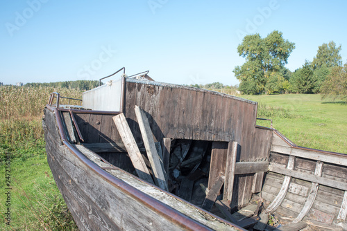 Very old wooden fishing boat with a hole aground on the grass. Blue sky, sunney day. Ancient fishing boat made of wood close up. Travel background. Place for text. Copy space. photo