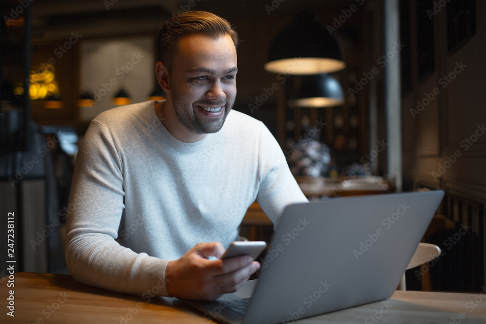 Young smiling businessman with laptop and smartphone on table. Young smiling businessman with laptop and smartphone on table.