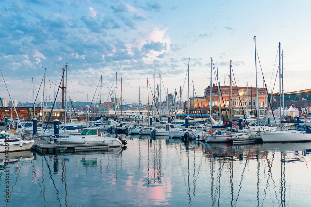 Paisaje en el que se ve un puerto deportivo con sus yates y sus barcos de vela atracados al atardecer