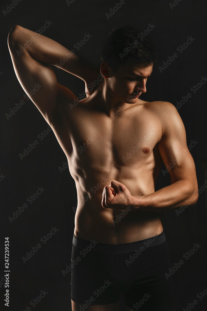 Naklejka premium Portrait of a man with a beautiful athletic body in a low key. Pumped up guy with a naked torso.