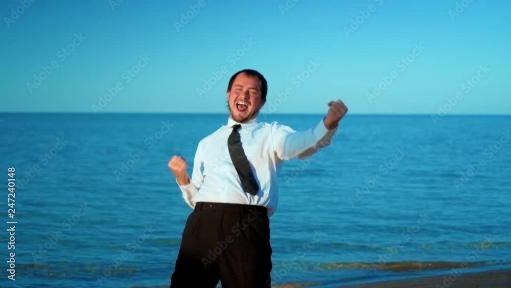 Excited businessman screaming and raising hands to the sky by the sea, slow motion Excited businessman screaming and raising hands to the sky by the sea, slow motion