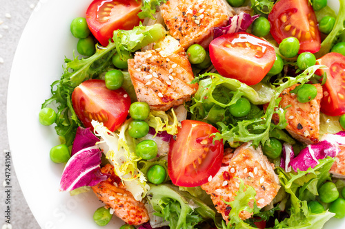 Healthy lunch vegetable salad with baked salmon fish, fresh green peas, lettuce and tomato. Top view