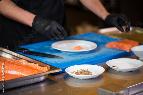 Theme cooking is a profession of cooking. Close-up of a Caucasian man's hand in a restaurant kitchen preparing red fish fillets salmon meat in black latex gloves uniform