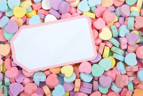 Brightly colored candy hearts, white card with pink border laying on top for copy space. Valentine's Day.