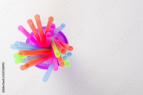 Bright multi-colored plastic tubules in a purple glass on a white background