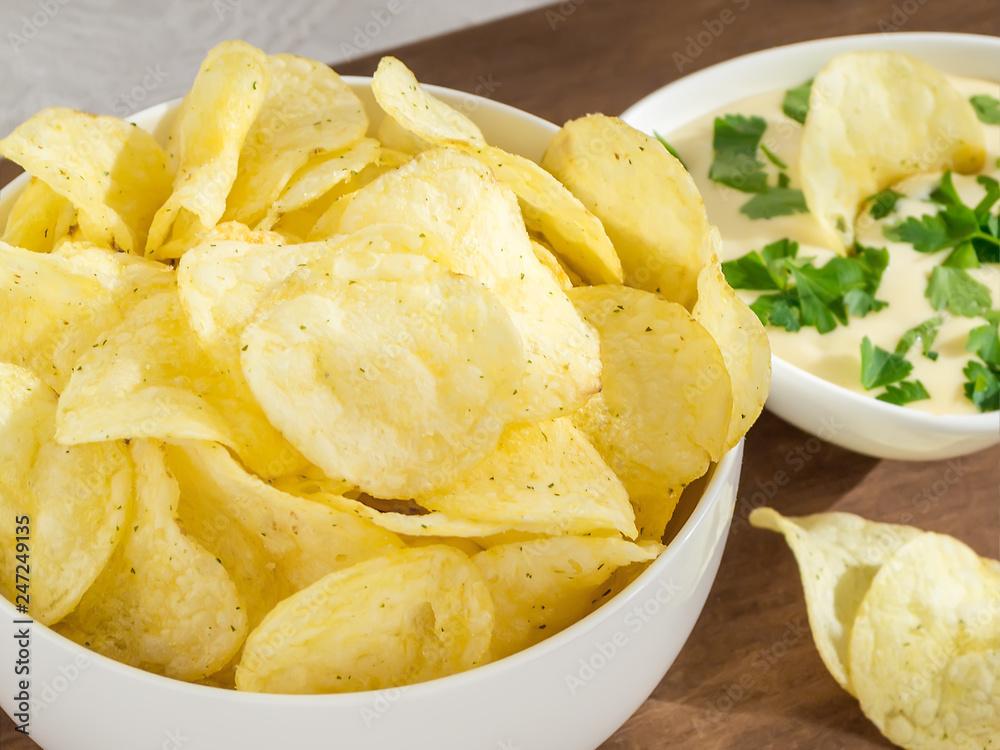 Crispy potato chips and fresh mayonnaise with parsley in a white bowls on a table. Fast food and tasty snack consept. Front view, close up, selective focus Crispy potato chips and fresh mayonnaise with parsley in a white bowls on a table. Fast food and tasty snack consept. Front view, close up, selective focus