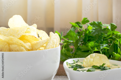 Crispy potato chips and fresh mayonnaise with parsley in a white bowls on a table. Fast food and tasty snack consept. Front view, close up, selective focus
