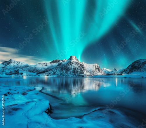 Fotografia Aurora borealis over snowy mountains, frozen sea coast, reflection in water at night