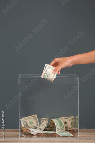 Cuadro en lienzo Woman putting money into donation box on table against grey background, closeup