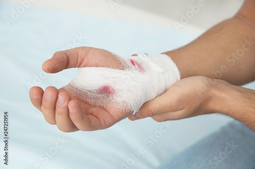 Young man with bandage on injured hand in clinic, closeup. First aid