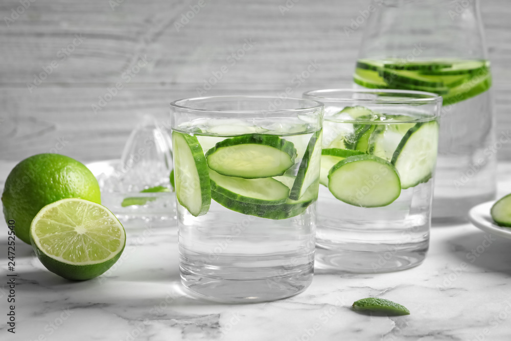 Glasses with fresh cucumber water on table against light background Glasses with fresh cucumber water on table against light background