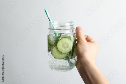 Young woman holding jar with fresh cucumber water on white background. Space for text