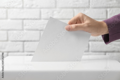 Woman putting her vote into ballot box against brick wall, closeup