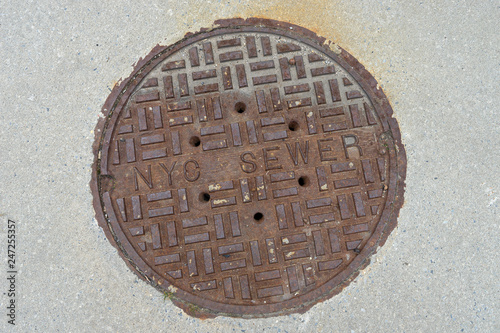 Old rusty sewer hatch on concrete surface, New York City.
