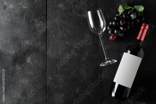 Red wine bottle with wine glass and grapes on dark wooden table flat lay from above