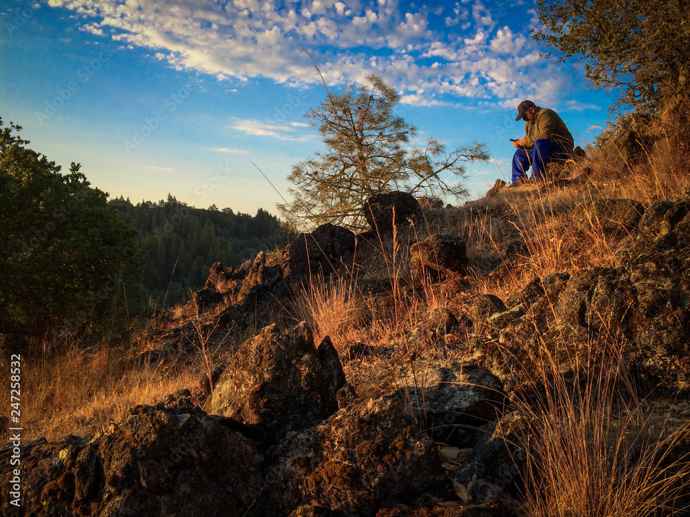 Man sitting on rocky hill at sunrise Man sitting on rocky hill at sunrise