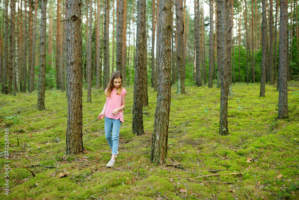 Cute young girl having fun during forest hike on beautiful summer day. Active family leisure.
