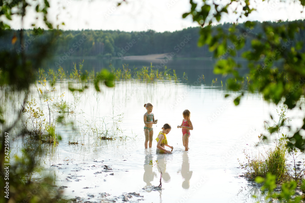 Three young sisters taking healing mud baths on lake Gela near Vilnius, Lithuania. Children having fun with mud. Three young sisters taking healing mud baths on lake Gela near Vilnius, Lithuania. Children having fun with mud.