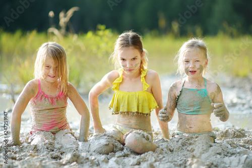 Three young sisters taking healing mud baths on lake Gela near Vilnius, Lithuania. Children having fun with mud.