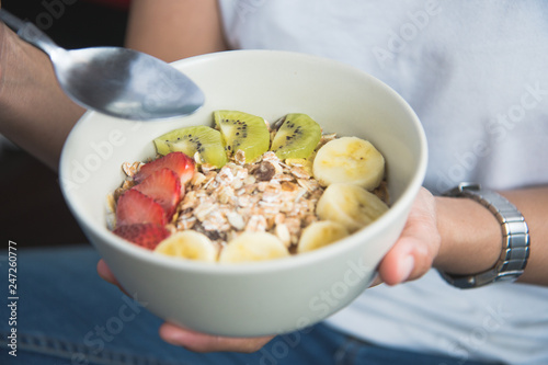 Eating healthy breakfast concept. Woman holding bowl of cereal and granola and variety fruits and glass of milk on th floor in the morning at home.