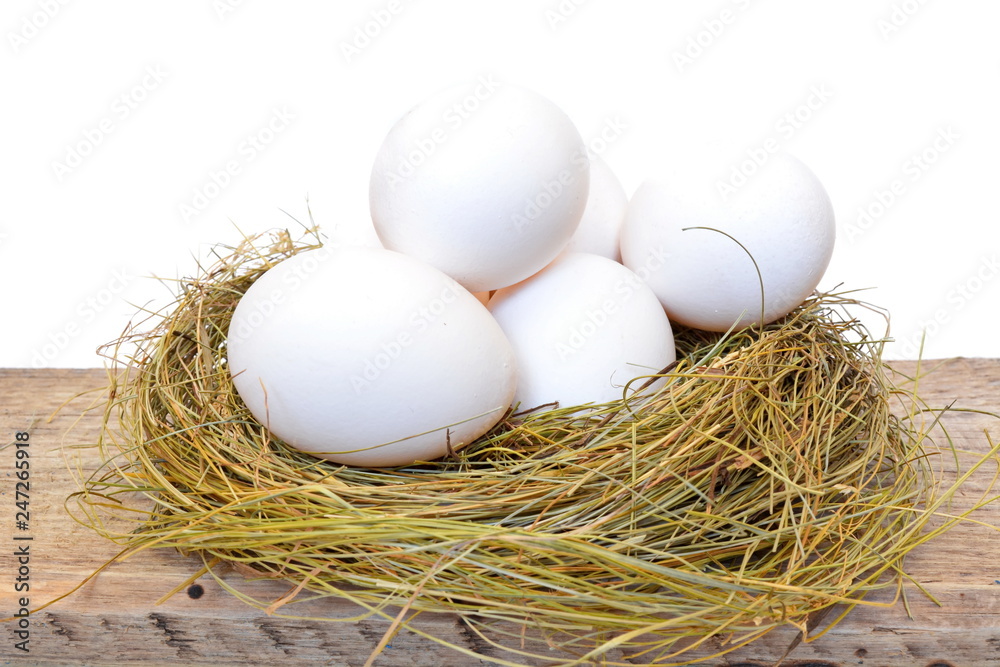 Heap white chicken eggs in a straw nest on rough wooden board on white background Heap white chicken eggs in a straw nest on rough wooden board on white background