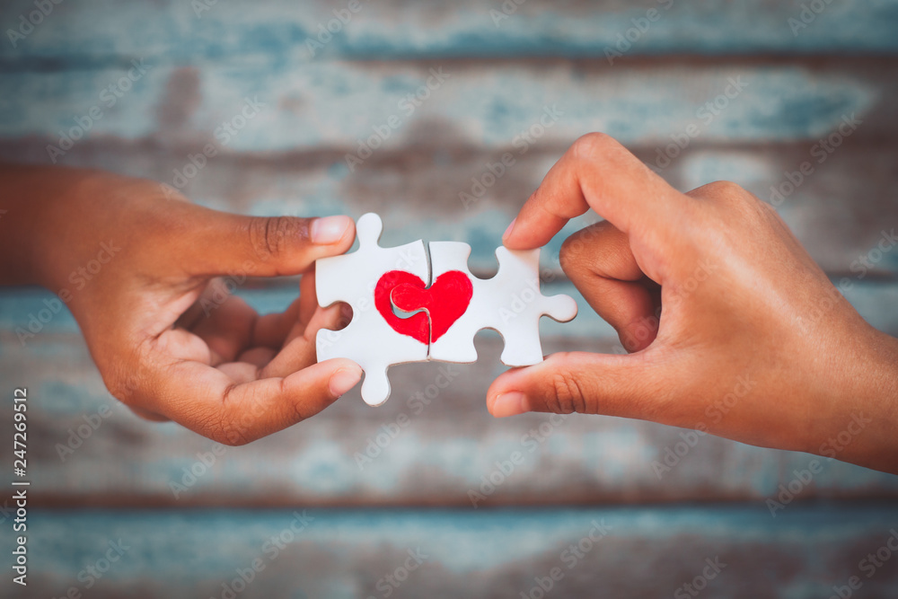 Two kid hands connecting couple jigsaw puzzle piece with drawn red heart
