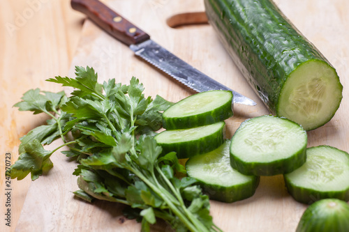 cutted cucumber and parsley on wooden cutting board with knife, selective focus, horizontal