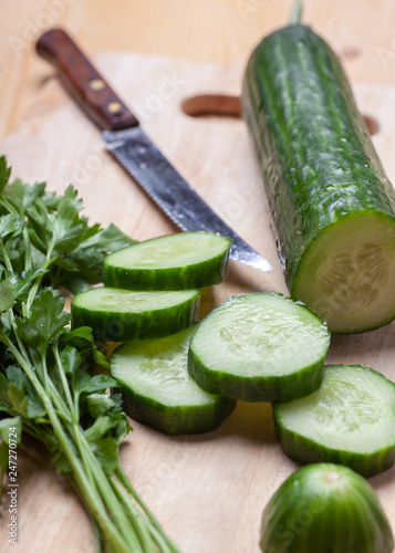 cucumber slices and parsley on wooden cutting board with knife, selective focus, vertical