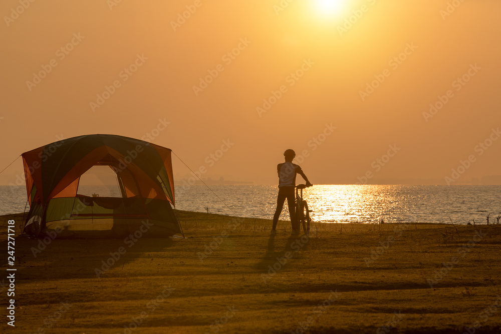 Camping tent at the lakeside during sunrise and  a man with bicycle enjoying with the nature and good weather